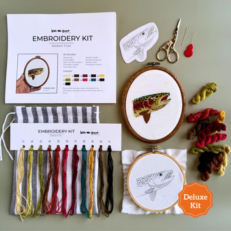 May include: An embroidery kit featuring a rainbow trout pattern, including a wooden hoop with a finished trout design, a second hoop with a printed trout outline, embroidery floss in various colors, scissors, needles, and instructional paper.