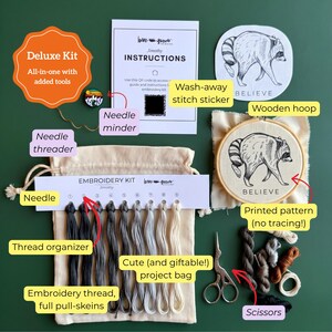 May include: A deluxe embroidery kit containing a wooden hoop with a raccoon pattern, a needle minder, a wash-away stitch sticker, a thread organizer with nine shades of embroidery thread, a needle threader, scissors, and a beige project bag.