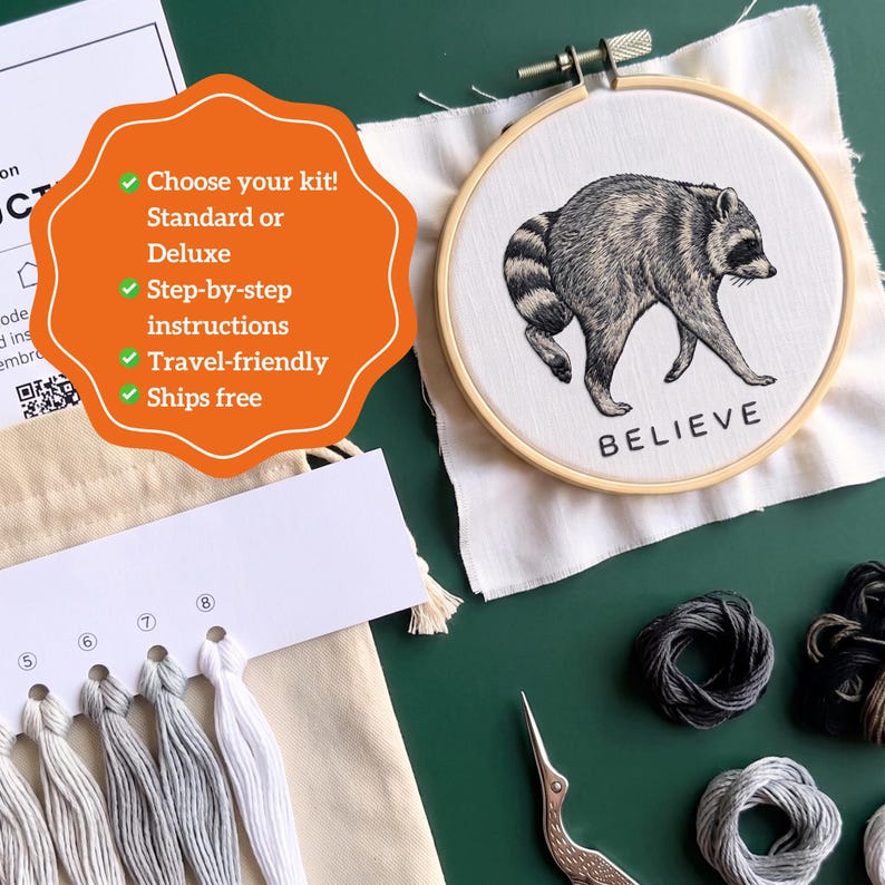 May include: An embroidery kit featuring a wooden hoop with a white fabric panel displaying a black ink illustration of a raccoon and the word BELIEVE. Includes a thread organizer with numbered white and gray embroidery floss and a metal crane scissor.