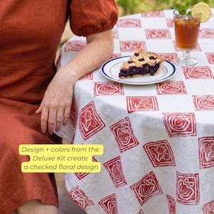May include: A white tablecloth with a red floral pattern covers a round table. A slice of pie sits on a white plate with a blue rim. A glass of iced tea with a lemon slice and mint sprig is also on the table. The text on the image says "Design + colors from the Deluxe Kit create a checked floral design."