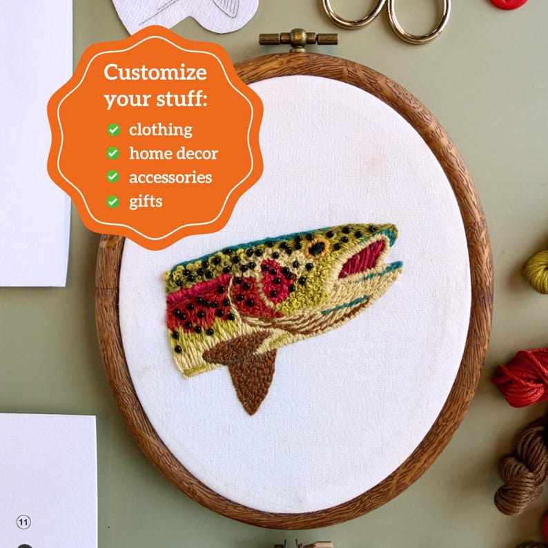 May include: An embroidery hoop containing white fabric with a stitched trout head design. The fish features green, yellow, and red thread with black spots. An orange graphic overlay reads: Customize your stuff: clothing, home decor, accessories, gifts.