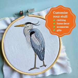 Pu&ograve; includere: Un telaio da ricamo in legno contenente tessuto bianco con un airone grigio ricamato a filo. Una sovrapposizione grafica arancione include il testo: Customize your stuff: clothing, home decor, accessories, gifts, ciascuno con una spunta verde.