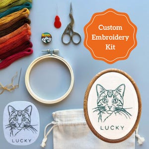 May include: A custom embroidery kit featuring a cat design. The kit includes embroidery threads in various colours, an embroidery hoop, scissors, a needle, and a canvas bag. The finished embroidery shows a cat portrait with the name "LUCKY". The kit is labelled "Custom Embroidery Kit".