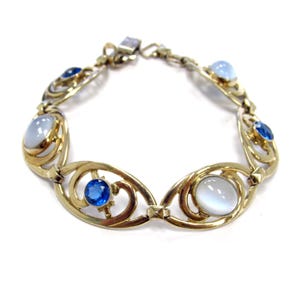 May include: A gold-toned bracelet featuring oval and circular links. The bracelet is adorned with blue and white gemstones. The design includes openwork details and a secure clasp. The bracelet is displayed against a white background.