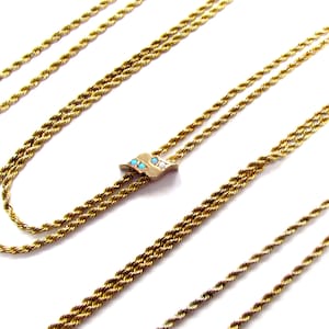 May include: A gold chain necklace with a small pendant featuring blue and white stones. The chain is made of two strands of rope-like links.