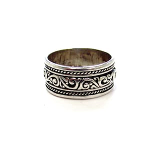 May include: A silver ring with an ornate, swirling pattern. The ring features a band of detailed scrollwork between two beaded borders. The design is symmetrical and wraps around the entire ring, creating a classic, elegant look.