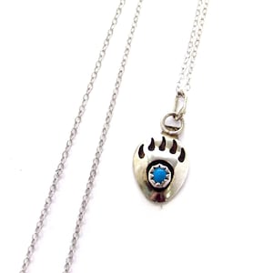 May include: A silver necklace with a bear paw pendant featuring a turquoise stone. The chain is a delicate silver chain.
