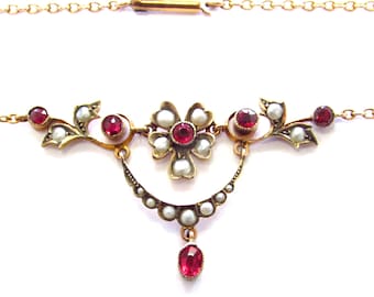 May include: A gold-toned necklace featuring a floral design with red gemstones and small white pearls. The necklace has a delicate chain and a pendant with a teardrop-shaped red gemstone. The design includes a flower and leaf motif.