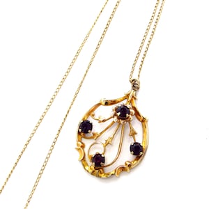 Op de afbeelding: Een goudkleurige hangerketting met een druppelvormig ontwerp. De hanger heeft vier donkerrode edelstenen en een sierlijk bloemmotief. De ketting is delicaat en goudkleurig, geschikt voor dagelijks gebruik.