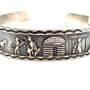 Puede incluir: Una pulsera de plata con un diseño detallado de vaqueros, caballos, una cabaña y una mujer con una cesta. La pulsera está hecha de plata de ley y tiene un acabado texturizado.