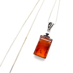 May include: A silver necklace with a rectangular amber pendant. The pendant is a warm, translucent orange-brown color, and the silver chain is delicate. The pendant is approximately 1 inch long.