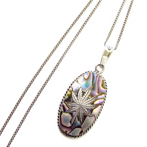 Puede incluir: Un collar de cadena de plata con un colgante que presenta un diseño de hoja de marihuana plateada sobre una concha de abulón iridiscente.