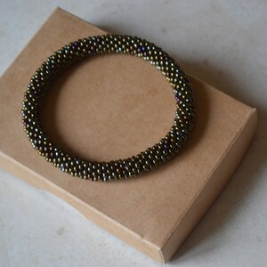 May include: A brown beaded bracelet with iridescent accents. The bracelet is on a brown cardboard box.