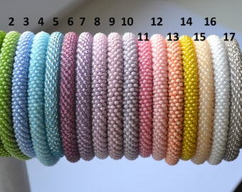 May include: A row of 17 colourful beaded bracelets, numbered 1 through 17. The bracelets are made of small, round beads in various colours, including green, blue, purple, pink, yellow, and white.