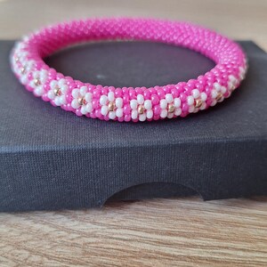 May include: A pink and white beaded bracelet with gold accents. The bracelet is made of small beads and has a floral pattern.