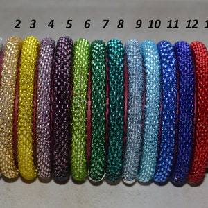 May include: Thirteen beaded bracelets in various colors, including silver, gold, yellow, purple, green, teal, blue, and red. The bracelets are numbered 1 through 13.