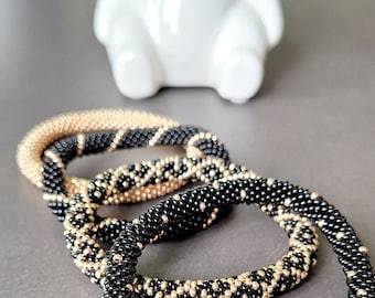 May include: Four beaded bracelets, two black and two black with gold accents. The bracelets are stacked on top of each other.