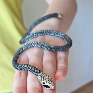 May include: A silver snake charm bracelet with black and silver beads. The bracelet is wrapped around a person's hand.