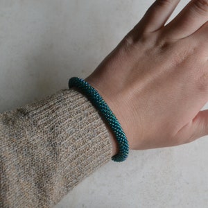May include: A teal blue beaded bracelet with a spiral design. The bracelet is worn on a person's wrist.