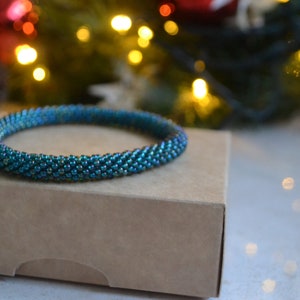 May include: A teal blue beaded bracelet on a brown box. The bracelet is made of small, iridescent beads.