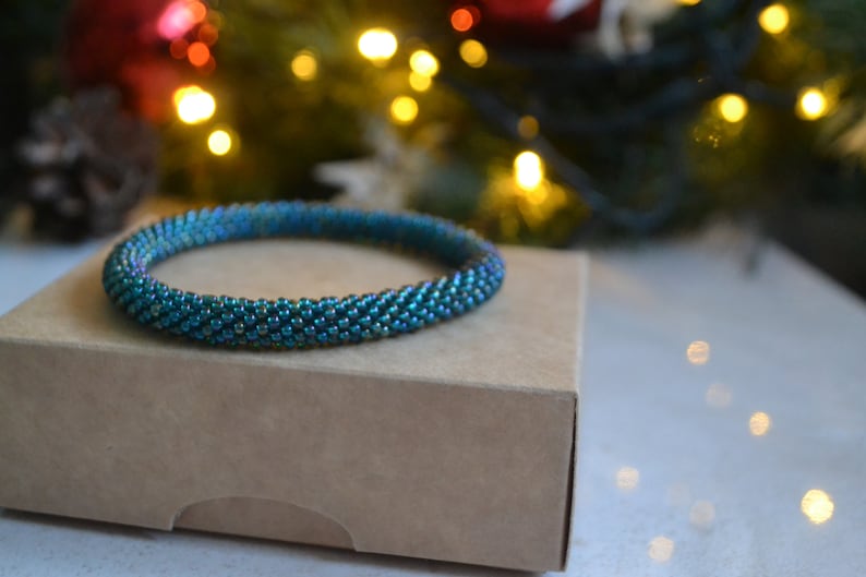 May include: A teal blue beaded bracelet on a brown box. The bracelet is made of small, iridescent beads.