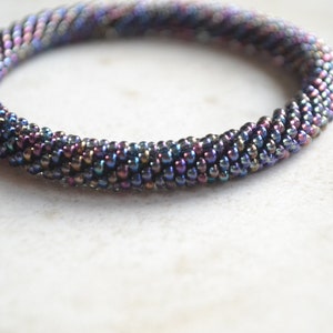 May include: A close-up of a beaded bracelet with a gradient of iridescent colors, ranging from purple to black.