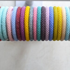 May include: A collection of colorful beaded bracelets in various shades of blue, pink, purple, yellow, and green. The bracelets are arranged in a row, with the darkest colors at the left and the lightest colors at the right.