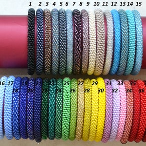 May include: A collection of 37 colourful beaded bracelets, arranged in two rows. The bracelets are made of small, round beads in various colours, including blue, green, yellow, pink, and red. The bracelets are numbered 1 through 37.