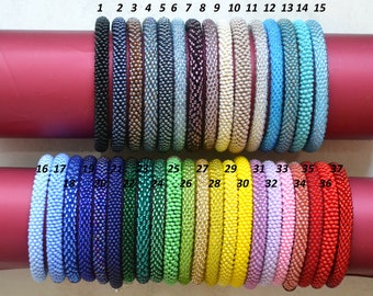 May include: A collection of 37 colourful beaded bracelets, arranged in two rows. The bracelets are made of small, round beads in various colours, including blue, green, yellow, pink, and red. The bracelets are numbered 1 through 37.