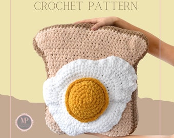 May include: Crochet pattern for a toast and fried egg pillow. The pillow is made of brown, white, and yellow yarn. The toast is brown and the egg is white with a yellow yolk.