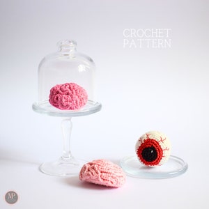 May include: Crochet pattern for a pink brain, a pink brain under a glass dome, and a white eyeball with a red iris and black pupil.