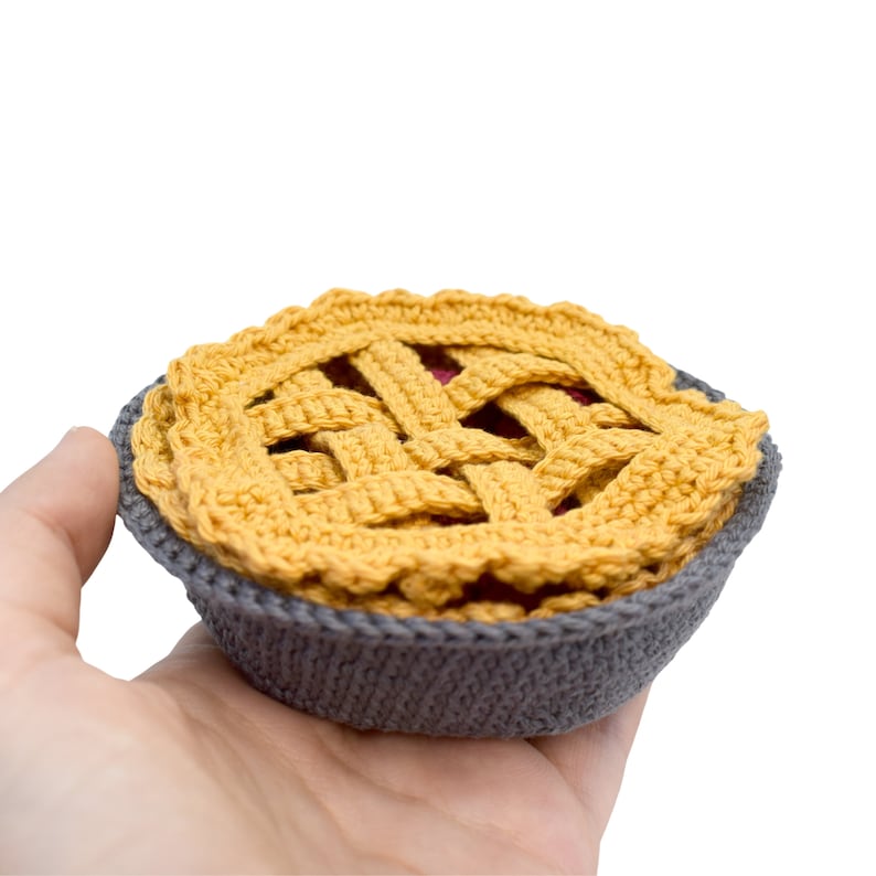 Puede incluir: Un pastel de ganchillo hecho de hilo amarillo en un molde para pastel de ganchillo gris.