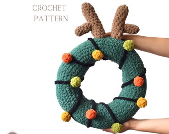 Könnte beinhalten: Ein grüner gehäkelter Weihnachtskranz mit braunen Geweih, schwarzem Garn und bunten Bommeln. Der Kranz ist mit Lichtern verziert und trägt den Text "CROCHET PATTERN" darüber.