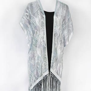May include: A light blue sheer kimono with a white floral pattern and white fringe trim.