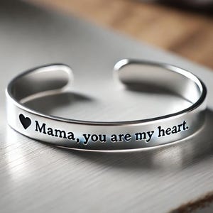 May include: Silver bangle bracelet with the inscription "Mama, you are my heart." and a small heart cutout.