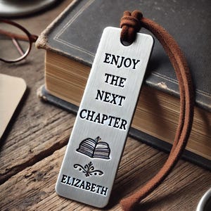 May include: Silver bookmark with a brown leather cord. The bookmark has the text "Enjoy the next chapter" and a small book illustration. The name "Elizabeth" is engraved at the bottom.
