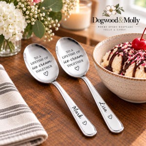 May include: Two polished silver-toned metal spoons featuring the engraved text TO A LIFETIME OF ice cream TOGETHER with a heart symbol on the bowl. The handles are personalized with the names Mark and Lisa, each followed by a small heart icon.