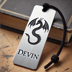 May include: Silver bookmark with a black dragon design and the name "DEVIN" engraved on it. The bookmark has a black cord.