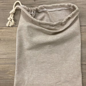 May include: A beige drawstring bag made of a soft, textured fabric. The bag has a white drawstring closure and is perfect for storing small items.
