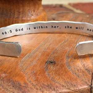 May include: Silver bracelet with the inscription "Psalm 46:5 God is within her, she will not fail".