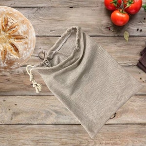May include: A round loaf of bread with a star-shaped design on top, sitting on a wooden surface. A beige cloth bag is lying on the surface next to the bread.
