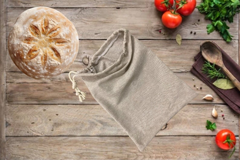 May include: A round loaf of bread with a star-shaped design on top, sitting on a wooden surface. A beige cloth bag is lying on the surface next to the bread.