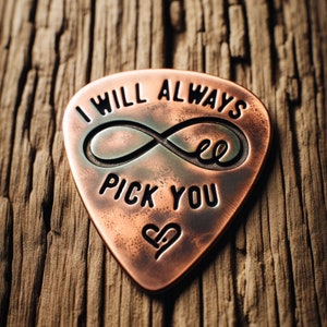 May include: A copper guitar pick with the words "I will always pick you" and an infinity symbol engraved on it. A heart is also engraved on the pick.