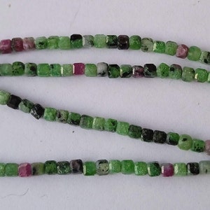 Könnte beinhalten: Eine Strähne aus grünen, schwarzen und rosafarbenen Edelsteinperlen. Die Perlen sind quadratisch und haben eine facettierte Oberfläche.