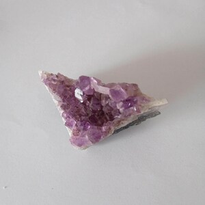 Peut inclure: Un amas de cristaux d'améthyste violette sur une matrice blanche. Les cristaux sont translucides et ont un léger éclat.