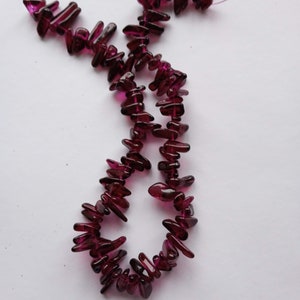 Peut inclure: Un brin de perles de pierres précieuses violet foncé, chaque perle est de forme longue et irrégulière, comme un éclat de verre. Les perles sont enfilées sur un fil transparent.