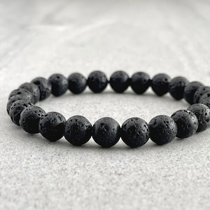 Peut inclure: Un bracelet en perles de roche volcanique noire. Les perles sont rondes et ont une surface rugueuse et texturée.