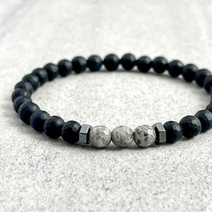 May include: A black beaded bracelet with three grey and white agate beads and two silver metal beads.