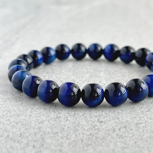 May include: A blue tiger's eye beaded bracelet. The beads are round and have a dark blue colour with a slight shimmer.