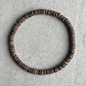 Könnte beinhalten: Ein braunes Holzperlenarmband mit schlichtem Design.